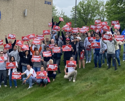 UAW members who work at the BMW-RDC in Nazareth, PA, at the Local 677 union hall holding red signs that say, "Saving the American Dream", "Stand Up", and "We Stand Together."