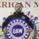 Photo of a Local 933 member holding a UAW sign with a "American Made, Union Proud" back drop.
