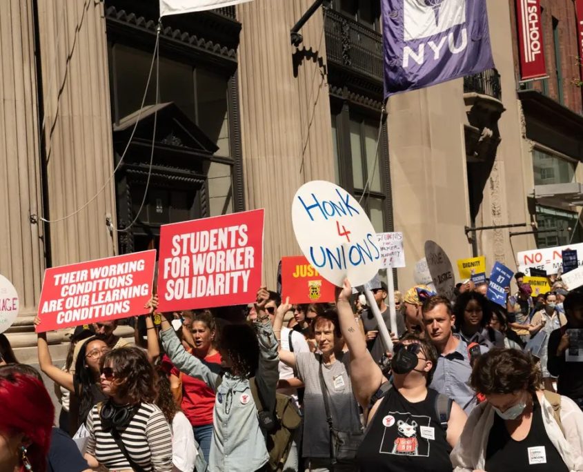 People rallying holding signs reading "students for worker solidarity" and "honk 4 unions"