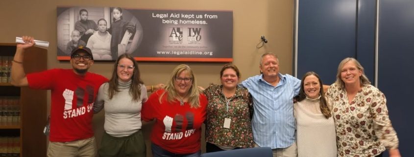 People posing in front of green house plants in office. People posing in front of legal aid sign in office location.