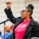 Member standing at mic wearing a red UAW t-shirt and black blazer, inside a UAW local union hall.