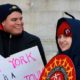 UAW members rally outside in winter attire, in front of building, holding signs