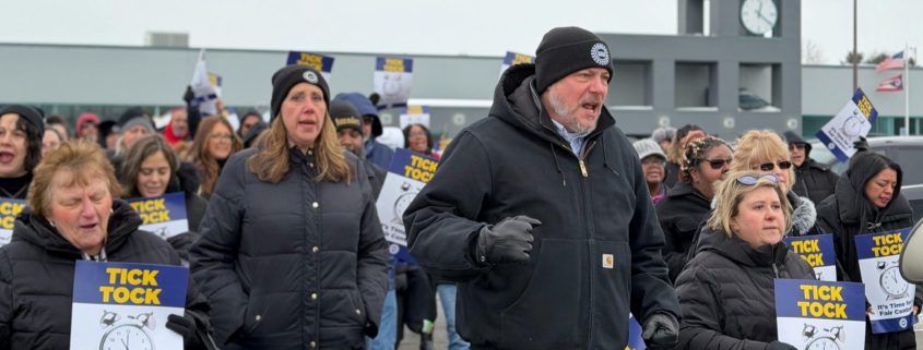 UAW Members picketing, wearing winter attire, holding signs, in front of county building,