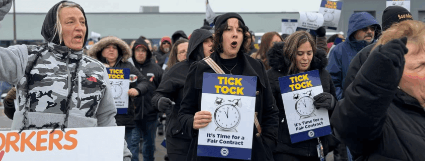 UAW member picketing in winter attire, holding winter coats, protesting.