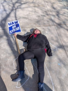 UAW TOP Member on strike lays on the ground where a body has been traced.